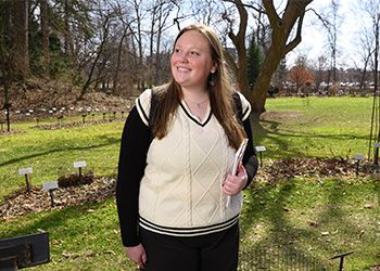 Beal Scholar Laura Perrin, wearing a backpack, standing in the Beal Botanical Garden, looking up and smiling.