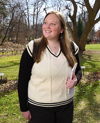 Beal Scholar Laura Perrin, wearing a backpack, standing in the Beal Botanical Garden, looking up and smiling.