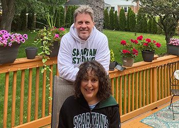 Greg Shafer and Bernadette Gongora pose for a photo on a wooden deck overlooking a garden.