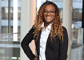 Oluwabusola Ajagbe wears a blazer and a flowered blouse and poses in a light-filled space in a campus building.