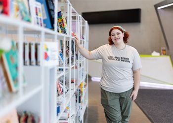 MJ Monteiro stands next to a colorful bookshelf in the Broad Art Museum.