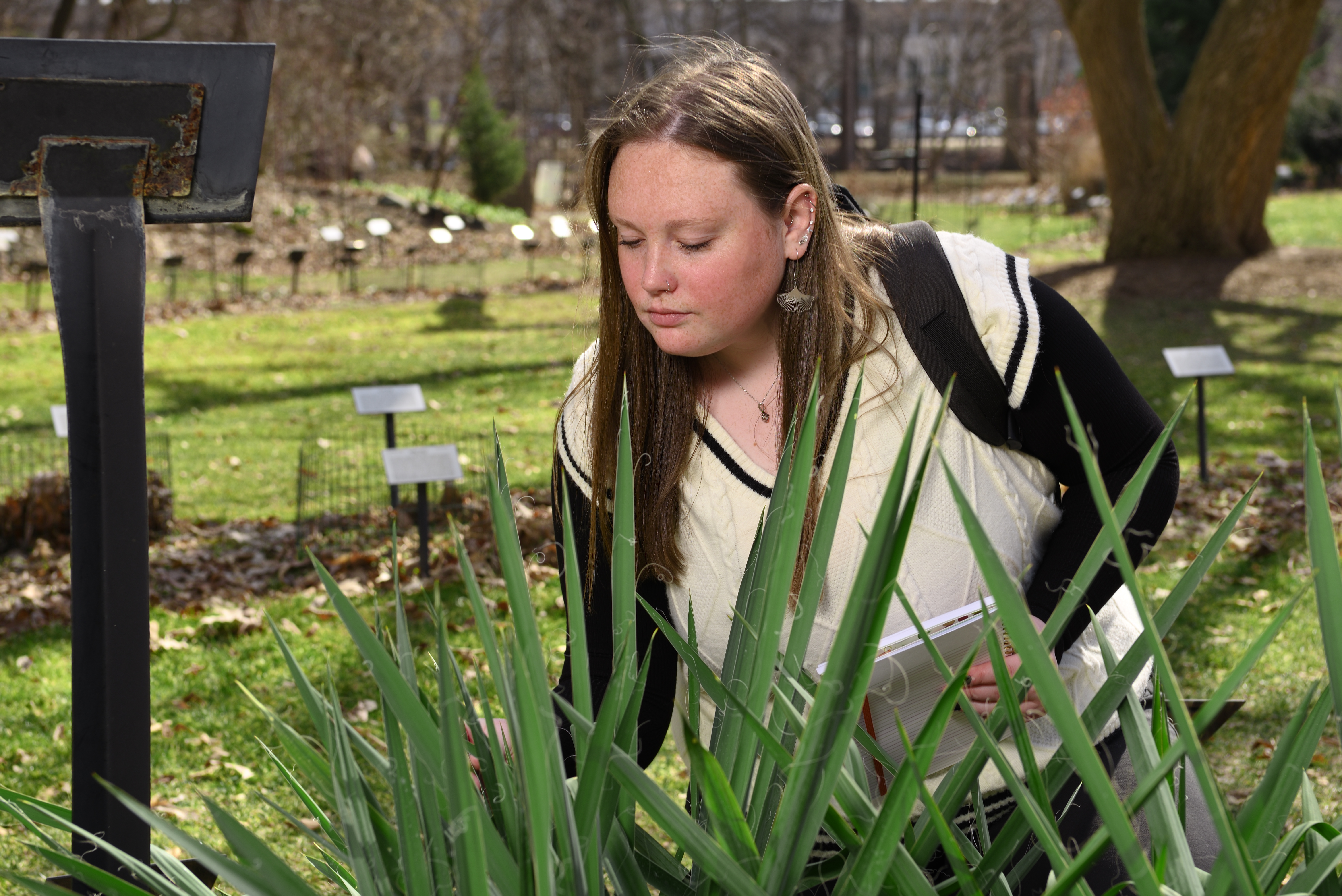 Beal Scholar Laura Perrin examines a plant in the garden, surrounded by greenery.